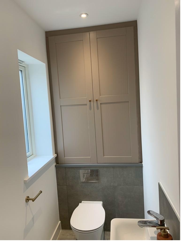 Bespoke over-toilet storage cupboard with two shaker-style doors in taupe grey paint and brass handles, Cambridge