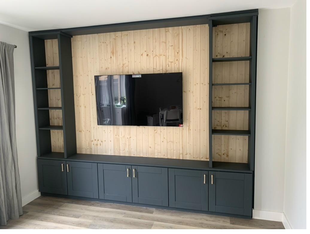 Completed bespoke media wall unit with vertical pine cladding, wall-mounted TV, dark grey shelving towers and shaker-style cabinet doors with brass handles, Cambridge
