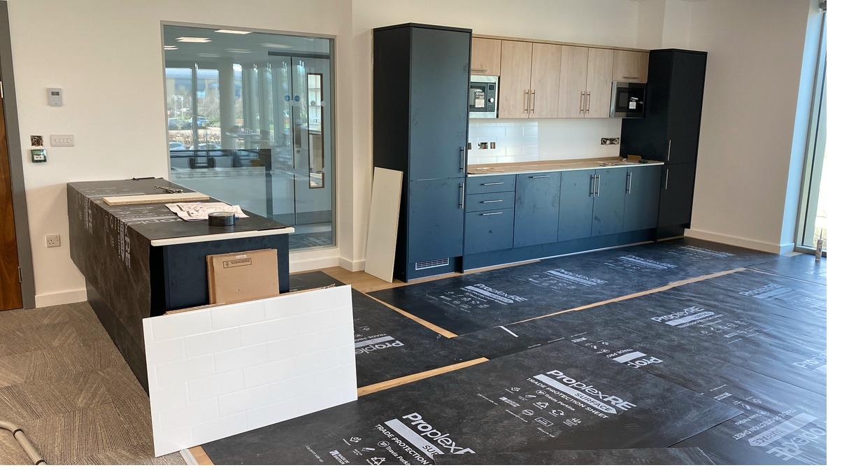 Completed commercial office kitchen with navy blue shaker cabinets, oak effect uppers, white metro tile splashback and integrated appliances — Cambridge area