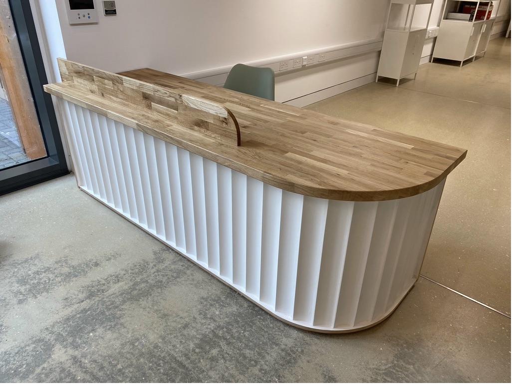 Completed bespoke curved reception desk with white fluted panel front, solid oak worktop and curved ends — finished installation in commercial space