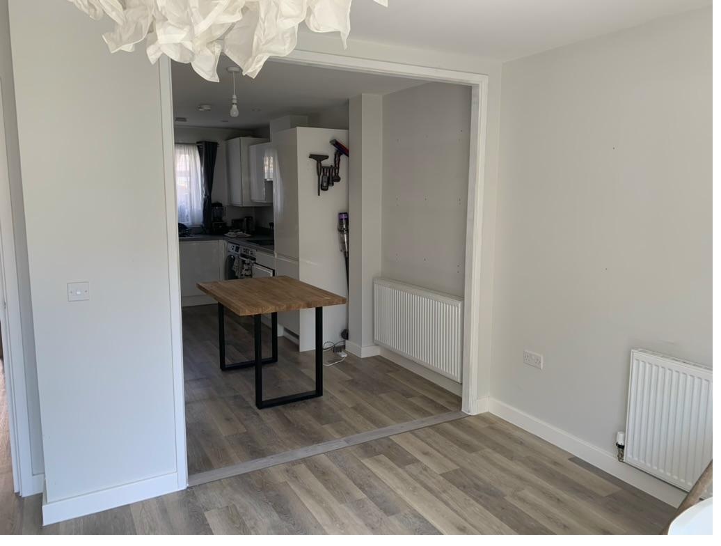 Completed open-plan living room and kitchen-diner connection after internal wall removal, with new plasterboard finish and oak dining table visible through opening — Cambridge