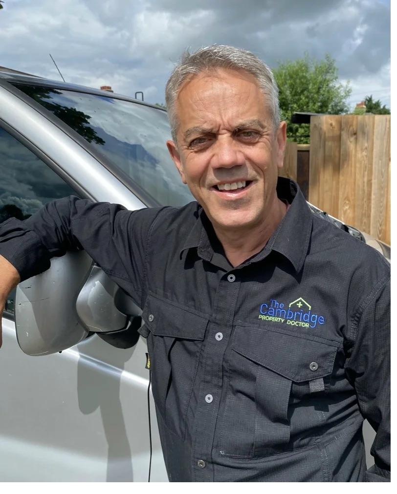 Simon, owner of Cambridge Property Doctor, wearing branded company shirt, leaning against work van — Cambridge